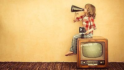 Una niña está sentada frente a un televisor sosteniendo un megáfono.