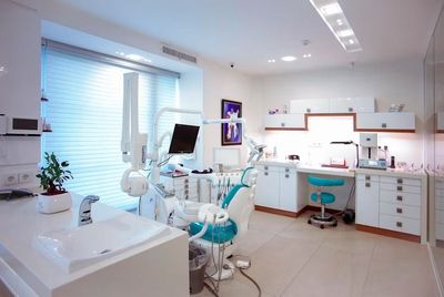 Clínica dental moderna con gabinetes blancos, sillón dental azul y equipo en una habitación luminosa.