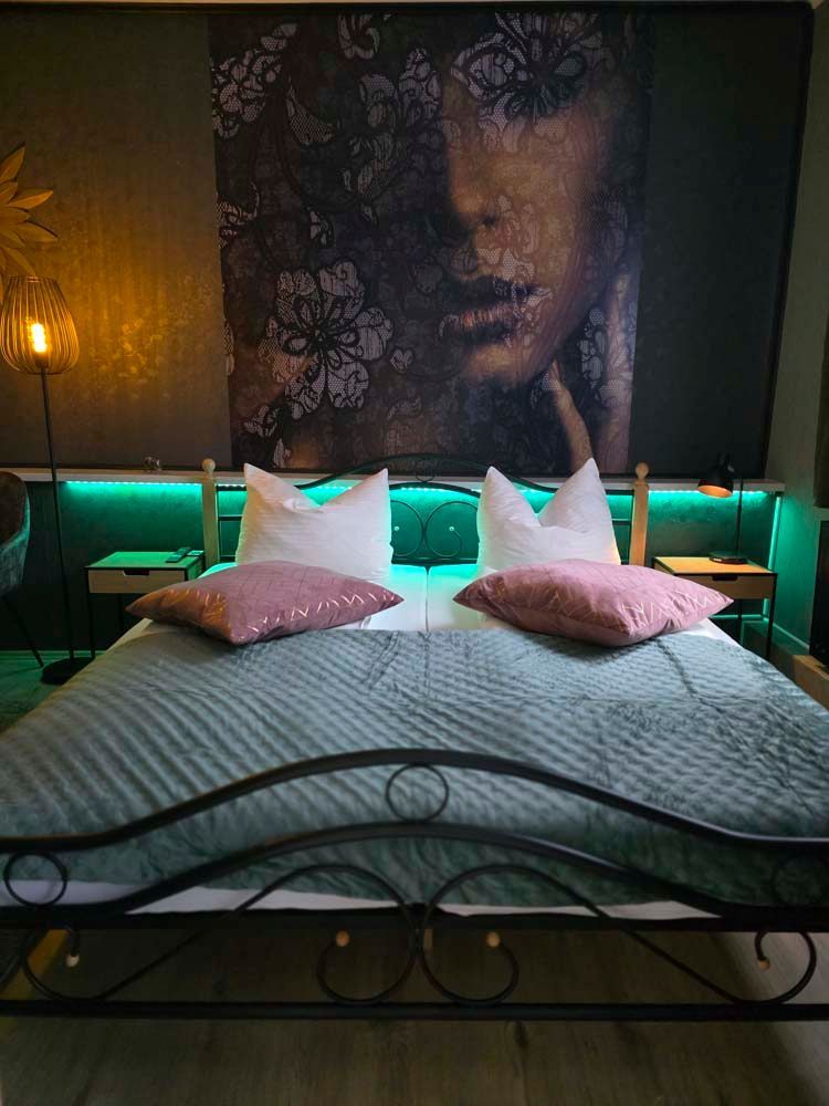 An der Wand über dem Bett hängt ein großes Gemälde mit dem Gesicht einer Frau.