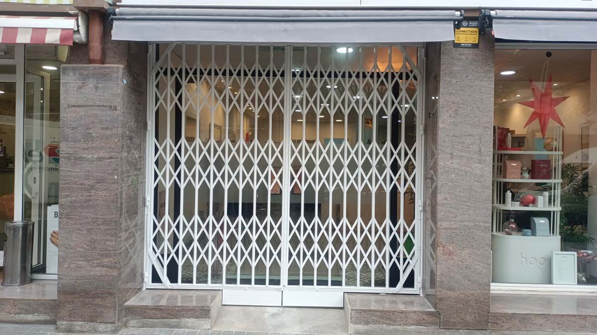 Puerta de seguridad blanca que cubre la entrada de una tienda. El escaparate es visible tras la puerta.