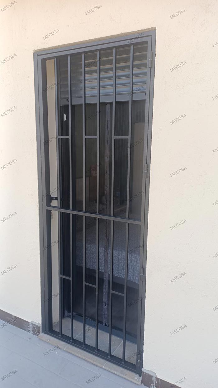 Puerta de seguridad metálica con barrotes verticales en una pared de color crema.