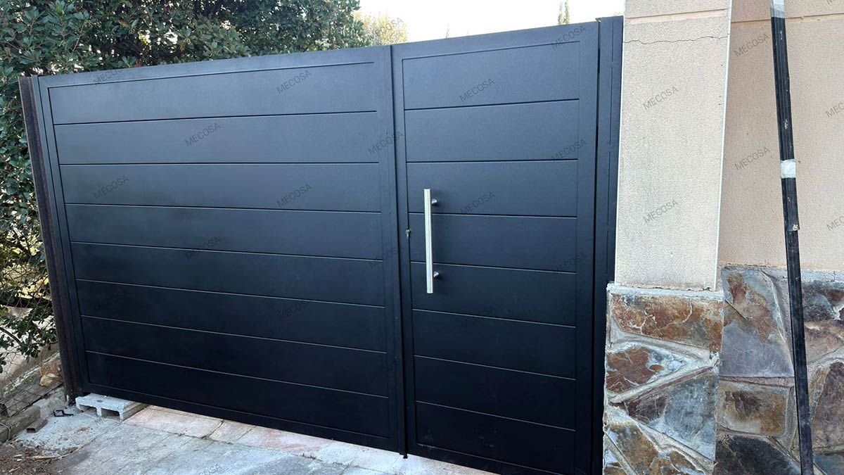 Puerta de metal negro con líneas horizontales y tirador plateado, engastada en estructura de piedra y estuco.