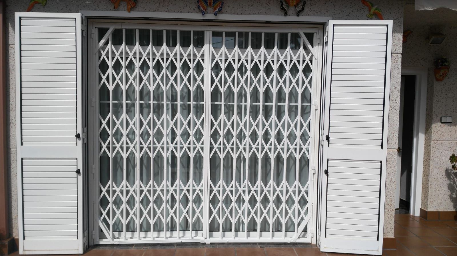 Una puerta blanca con contraventanas a los lados.