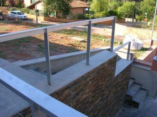Una escalera con barandilla de metal y una pared de piedra.