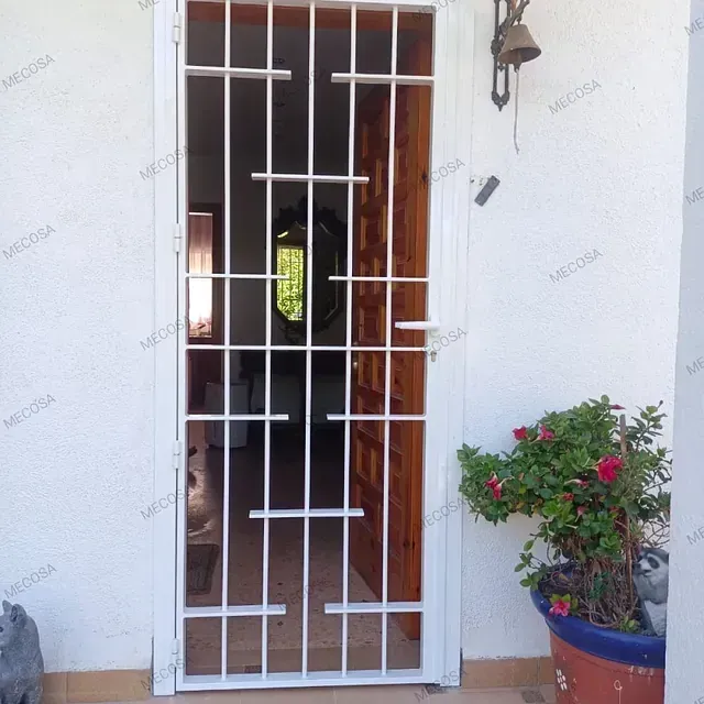 Una puerta con una reja de metal y una planta en maceta delante de ella.