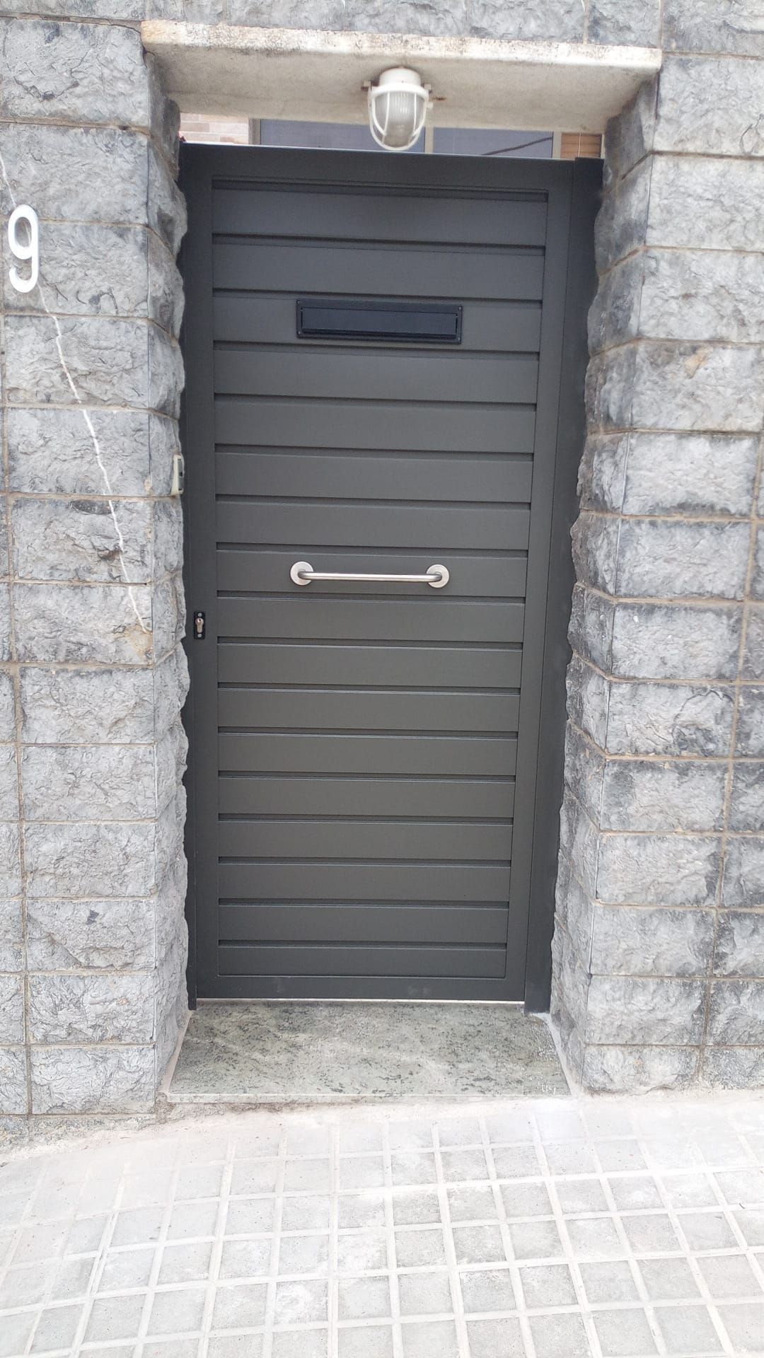 Una puerta negra está frente a una pared de ladrillos.