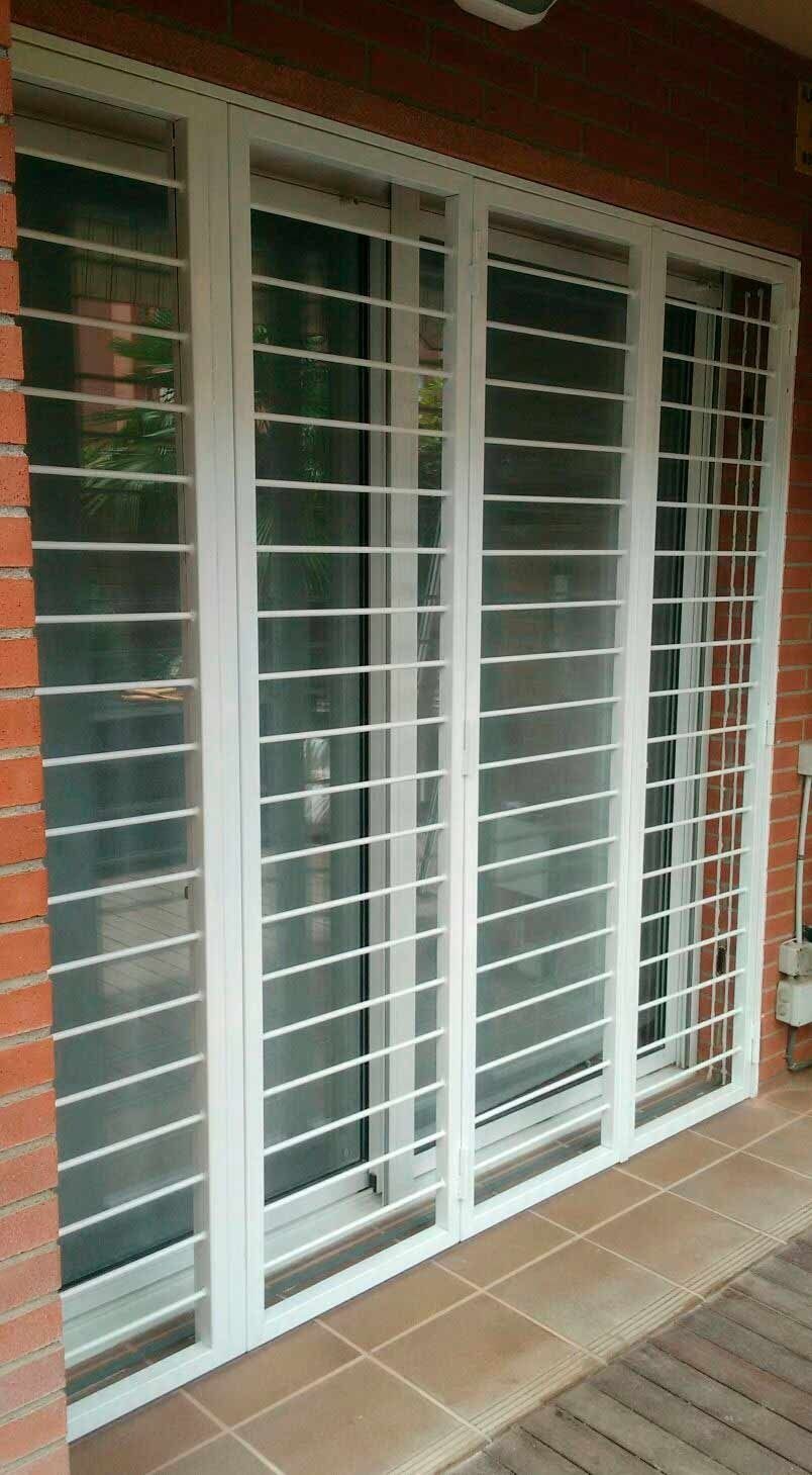 Una puerta corrediza de vidrio blanca con una barandilla de metal en una pared de ladrillos.