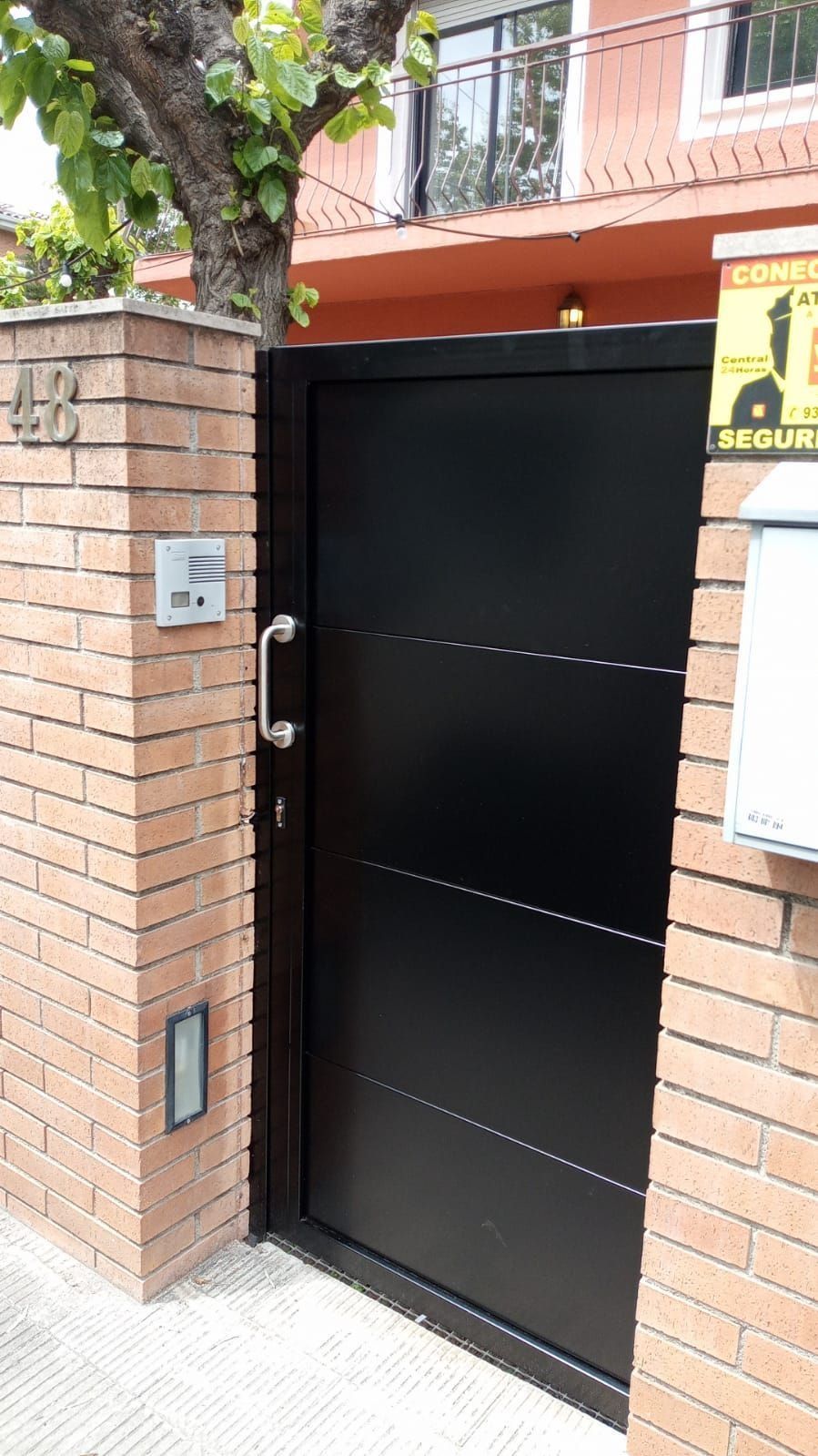 Una puerta negra está entre una pared de ladrillos y un edificio.