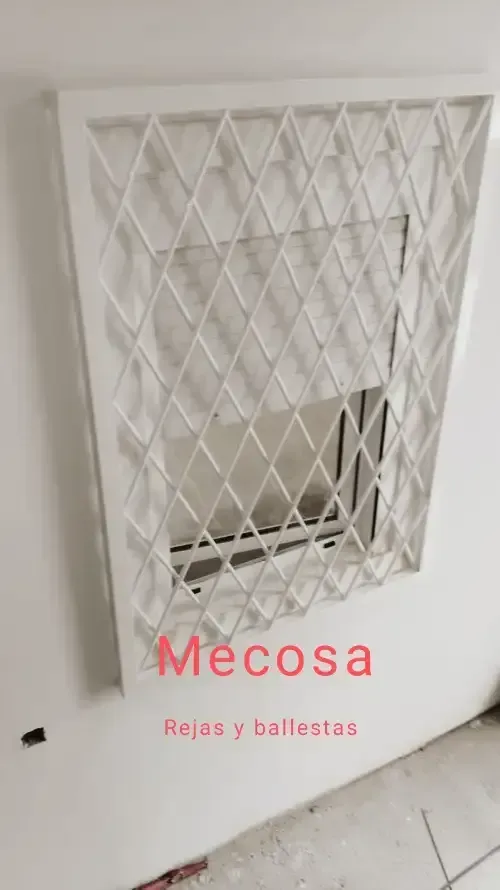 Una puerta blanca con una rejilla de metal está colgada en una pared blanca.