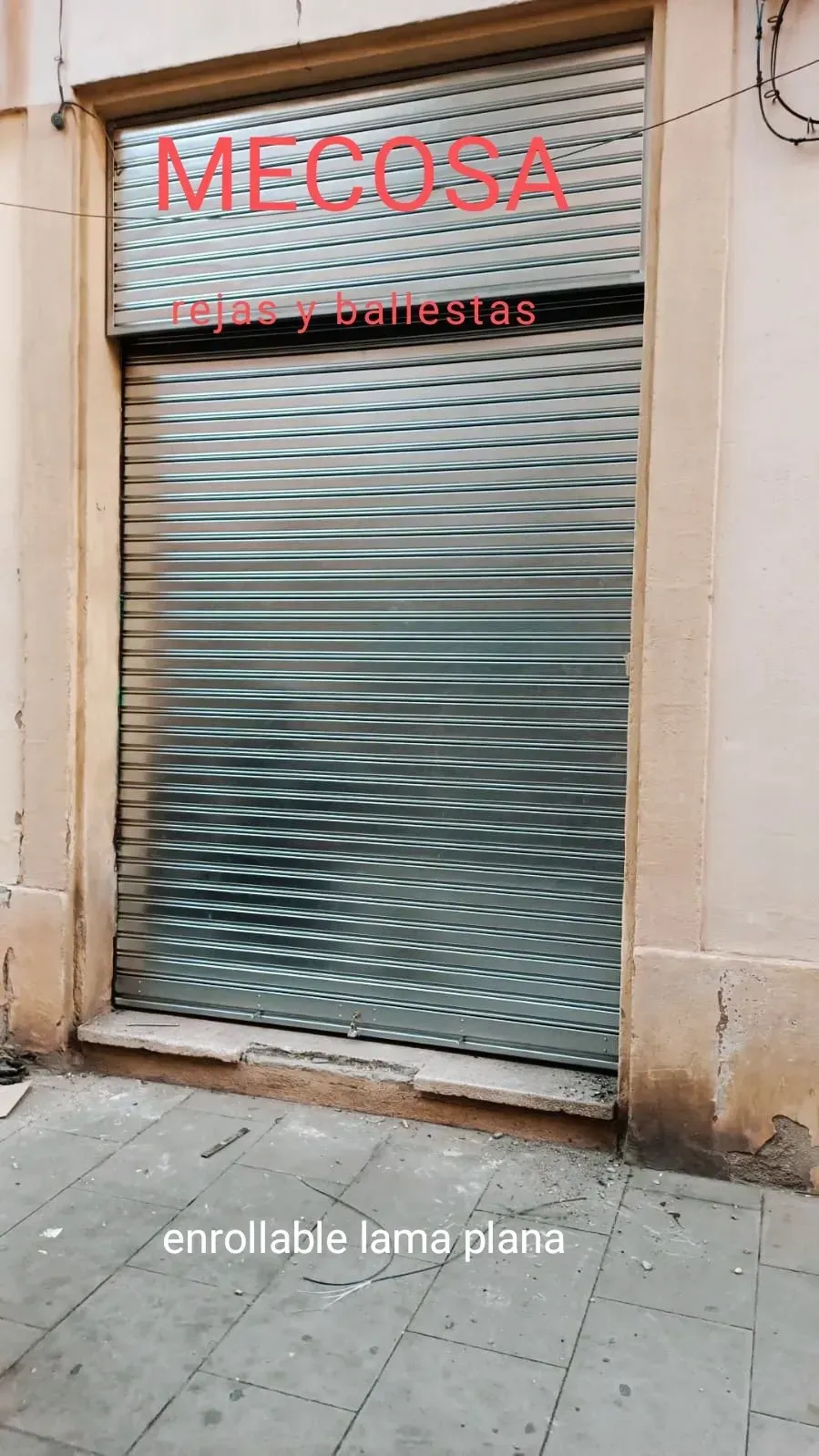 Un escaparate con una persiana metálica que dice mecosa.