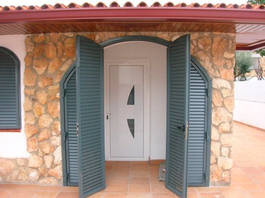 Un edificio de piedra con una puerta blanca y contraventanas verdes.