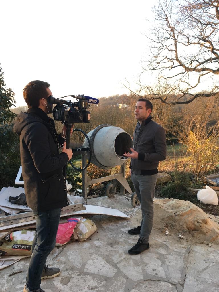 Deux hommes sur un chantier. L'un filme l'autre avec une caméra placée à côté d'une bétonnière.
