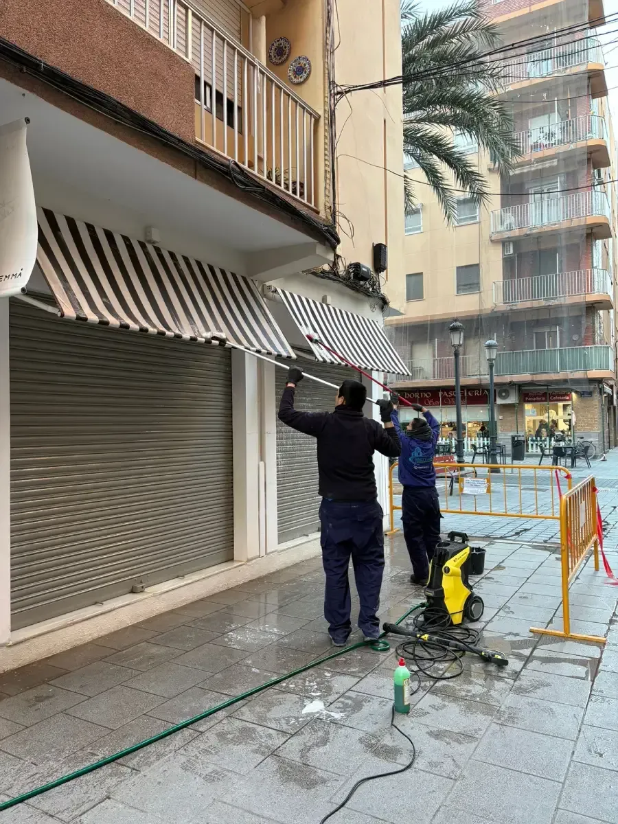 Dos trabajadores vestidos con ropa oscura utilizan hidrolimpiadoras de alta presión para limpiar