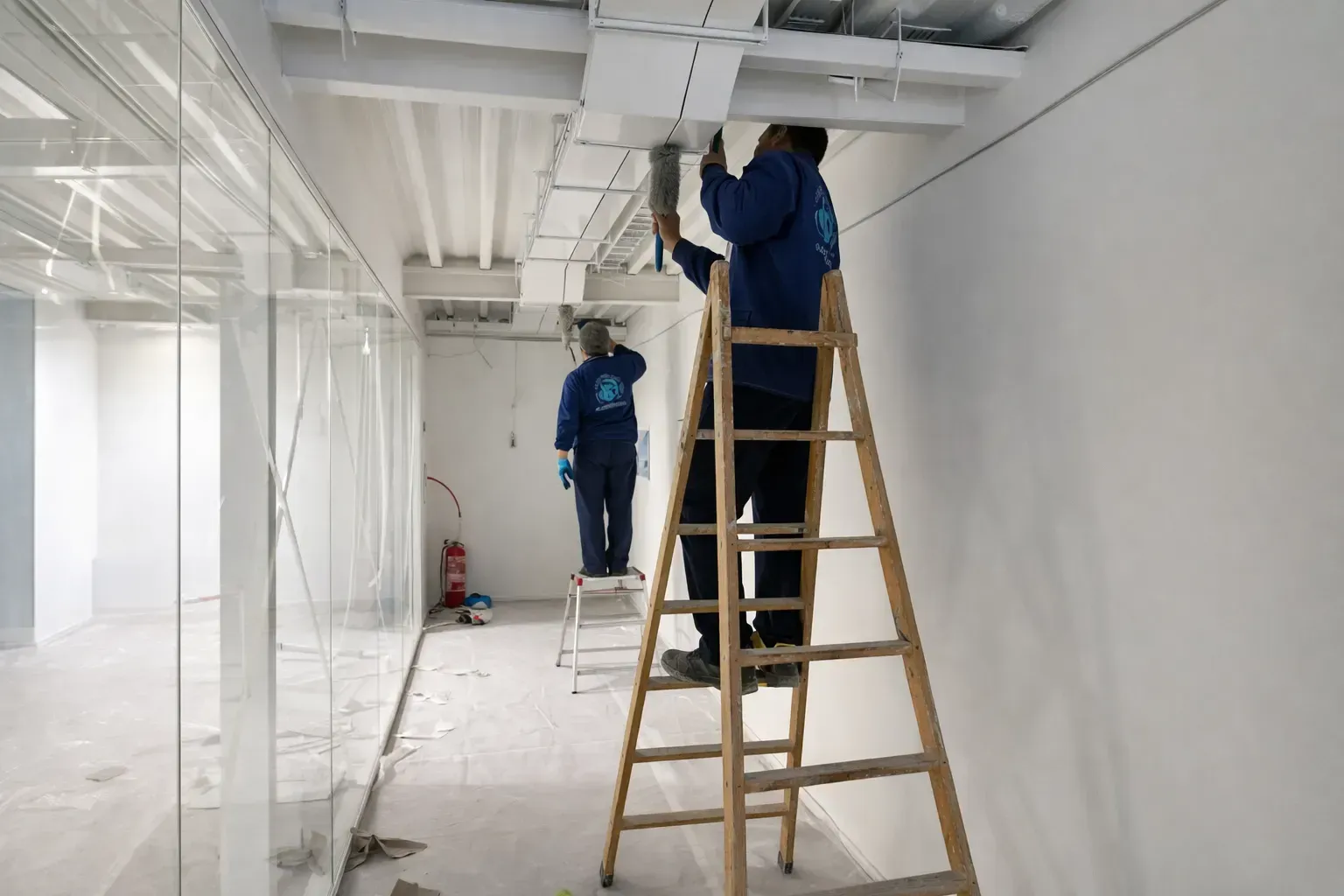 Dos trabajadores con uniformes azules están subidos a escaleras mientras instalan infraestructura