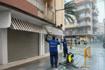 Una persona vestida con ropa de trabajo azul aspira la alfombra de un pasillo junto a un conjunto de puertas