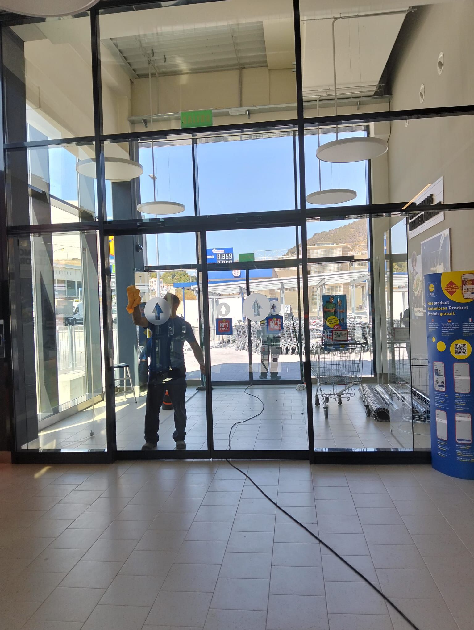 Mano usando una escobilla de goma para limpiar una ventana, con un paisaje urbano difuminado en el fondo.