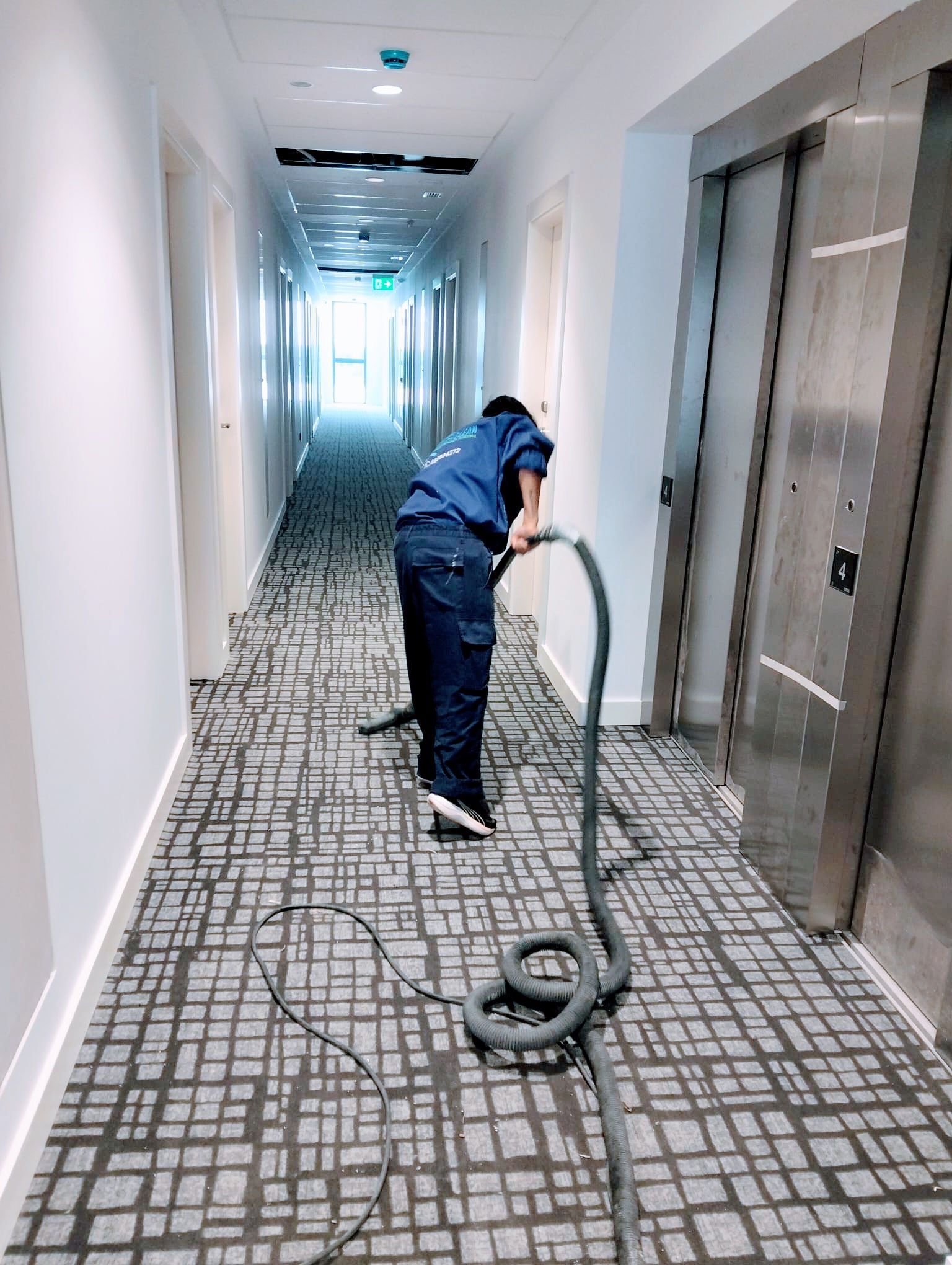 Persona aspirando una alfombra gris, levantando polvo.