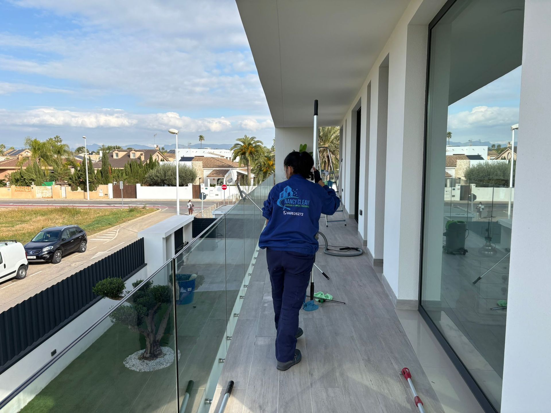 Una persona limpia una ventana con una escobilla de goma de mango largo. Edificio turquesa. Exterior.