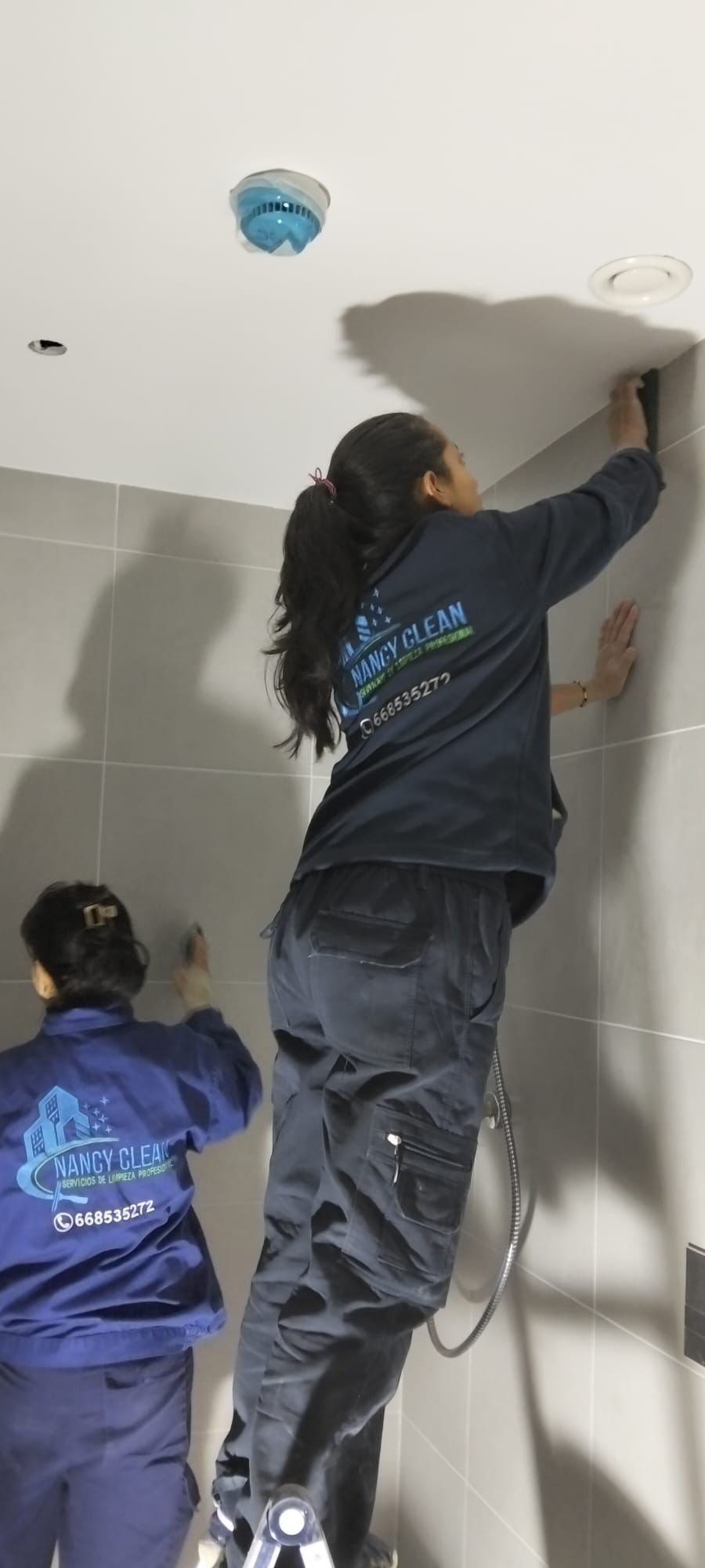 Una persona limpia una ventana con una escobilla de goma de mango largo. Edificio turquesa. Exterior.