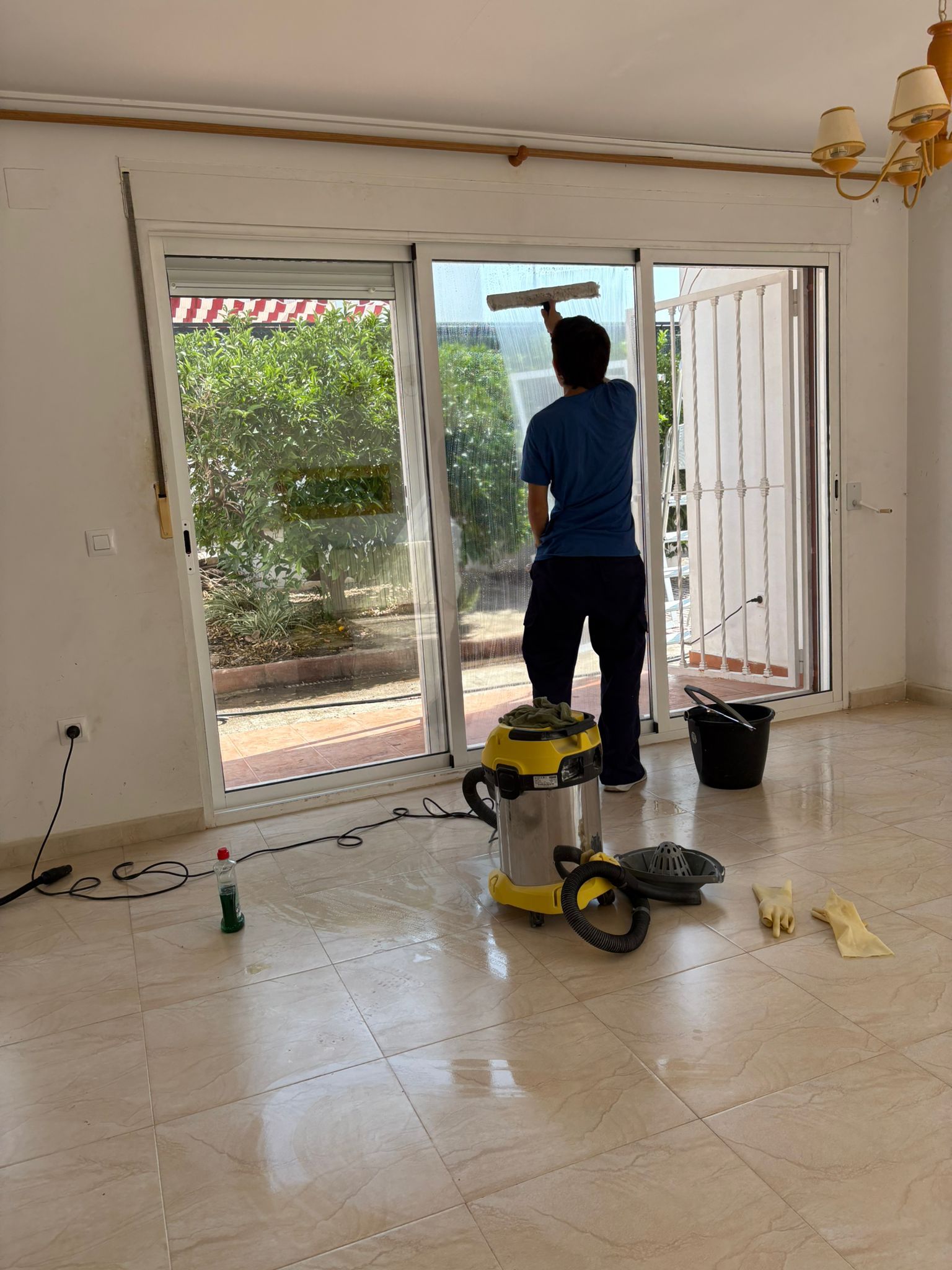 Mano usando una escobilla de goma para limpiar una ventana, con un paisaje urbano difuminado en el fondo.