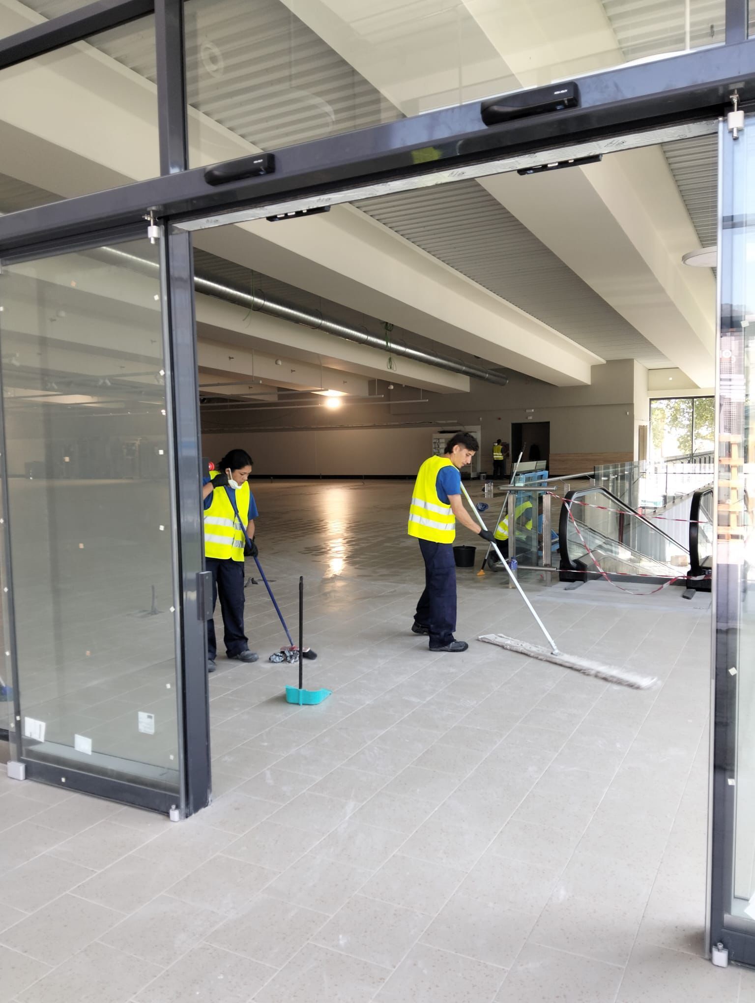 Dos personas con camisetas verdes y máscaras recogiendo basura en una playa con montañas de fondo.