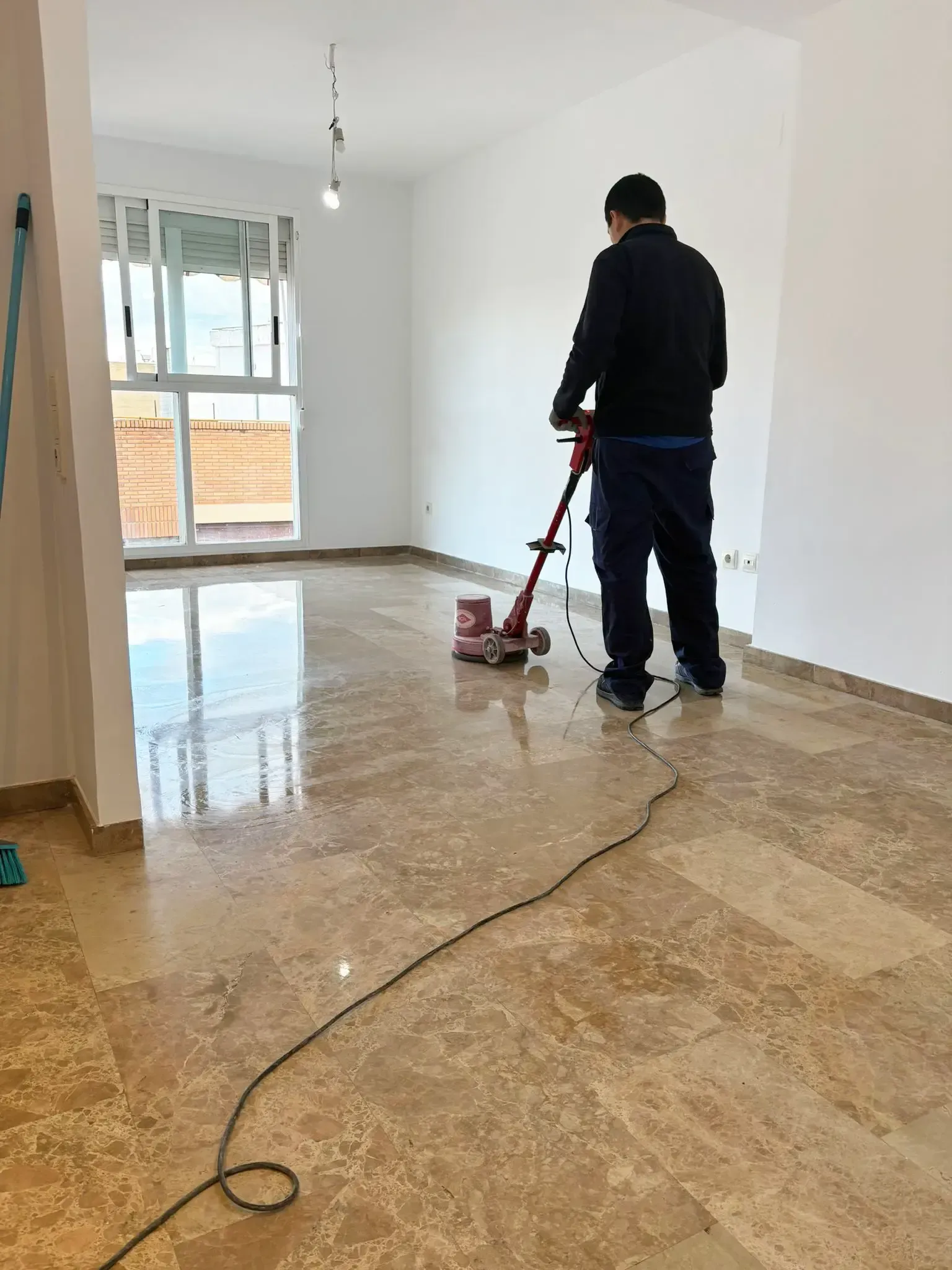 En una habitación luminosa, una persona vestida con ropa de trabajo pule un brillante suelo de mármol 