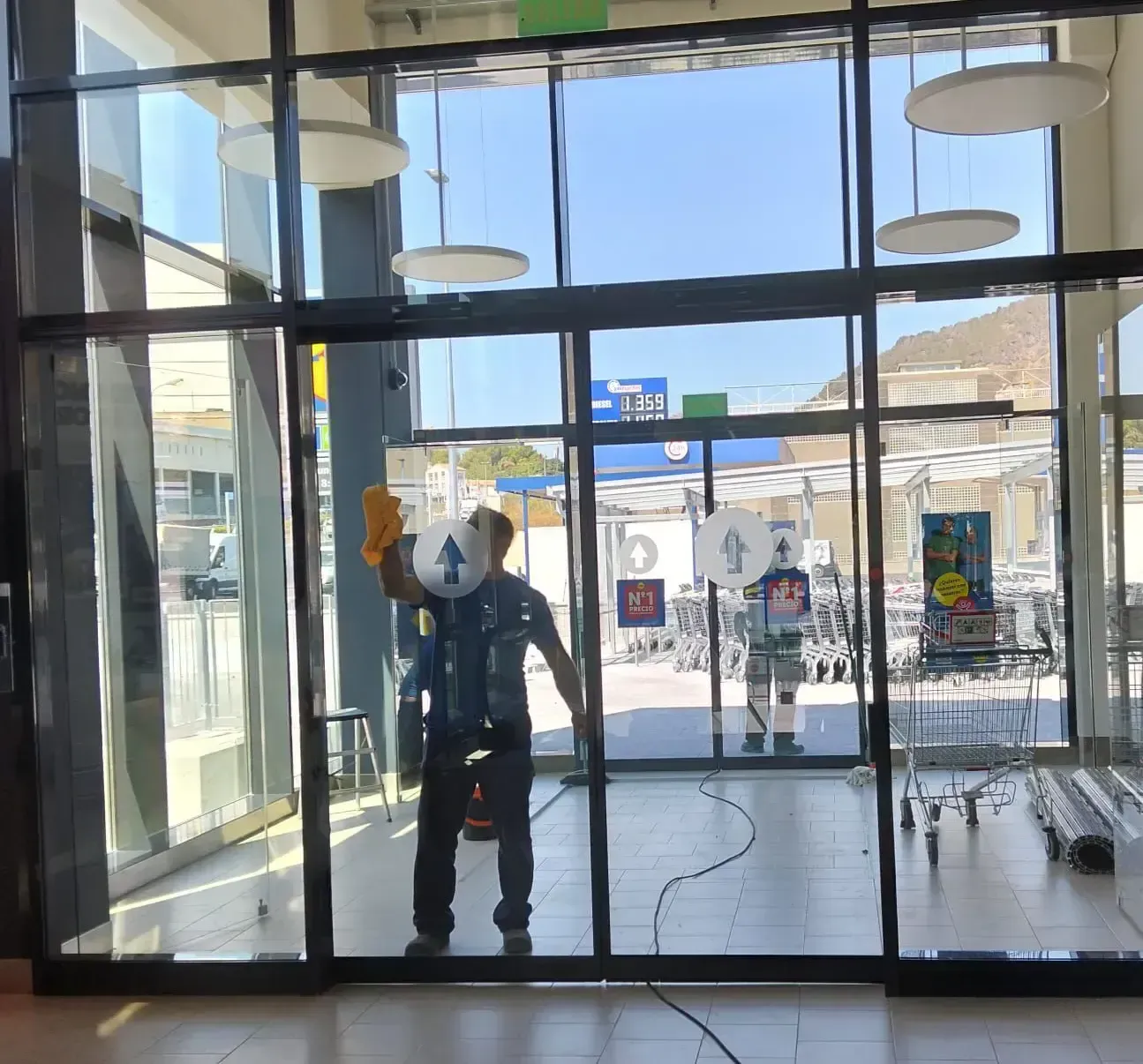 Una persona con uniforme azul utiliza una herramienta de mango largo para limpiar la barandilla de cristal