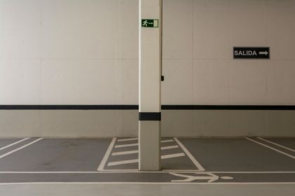 Obrero sobre un andamio móvil en un estacionamiento cubierto con marcas amarillas en el suelo.
