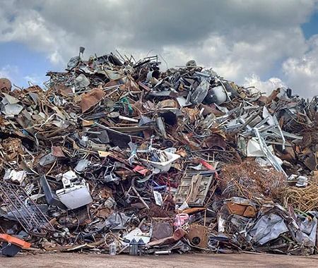 Montón de chatarra contra un cielo nublado. Diversos objetos metálicos se apilan, creando un gran montón.