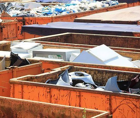 Contenedores metálicos de color naranja llenos de electrodomésticos desechados y otros residuos en un vertedero.