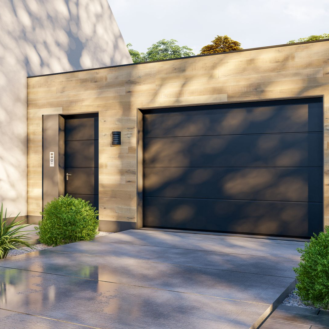 Extérieur d’une maison moderne beige avec une porte de garage noire et une entrée à côté d’une allée mouillée.