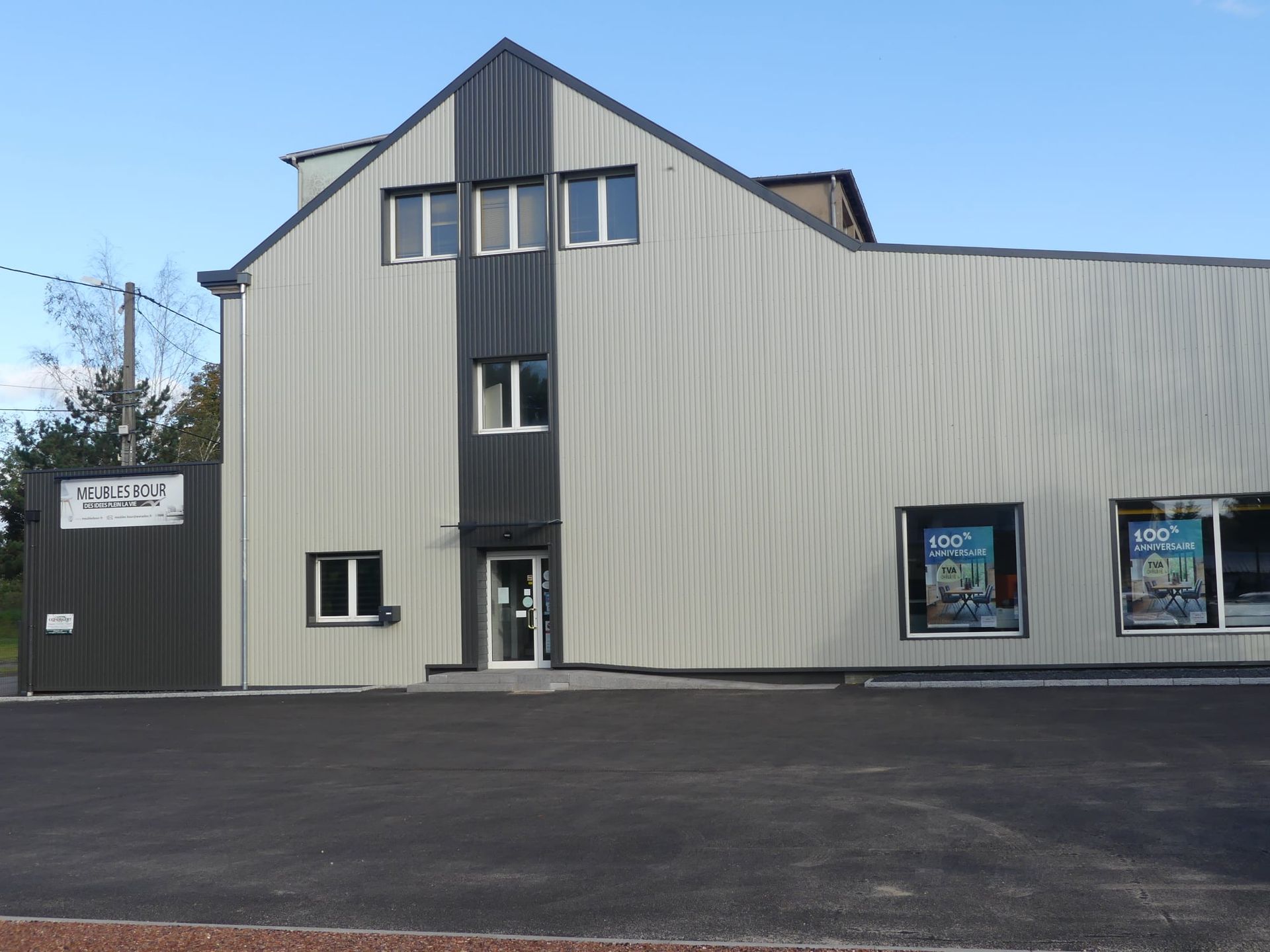 Bâtiment aux façades beiges, avec des encadrements de fenêtres bruns et un volet enroulé ; ciel bleu visible.