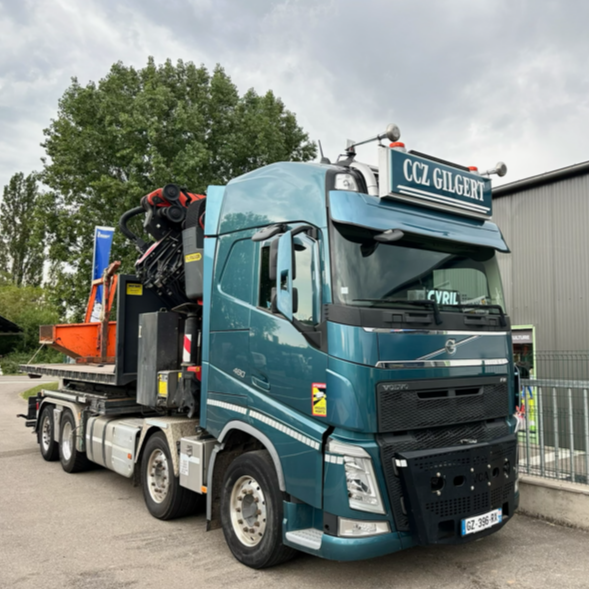 Camion Volvo turquoise avec grue, stationné devant un bâtiment. Logo CCZ Gilbert visible.