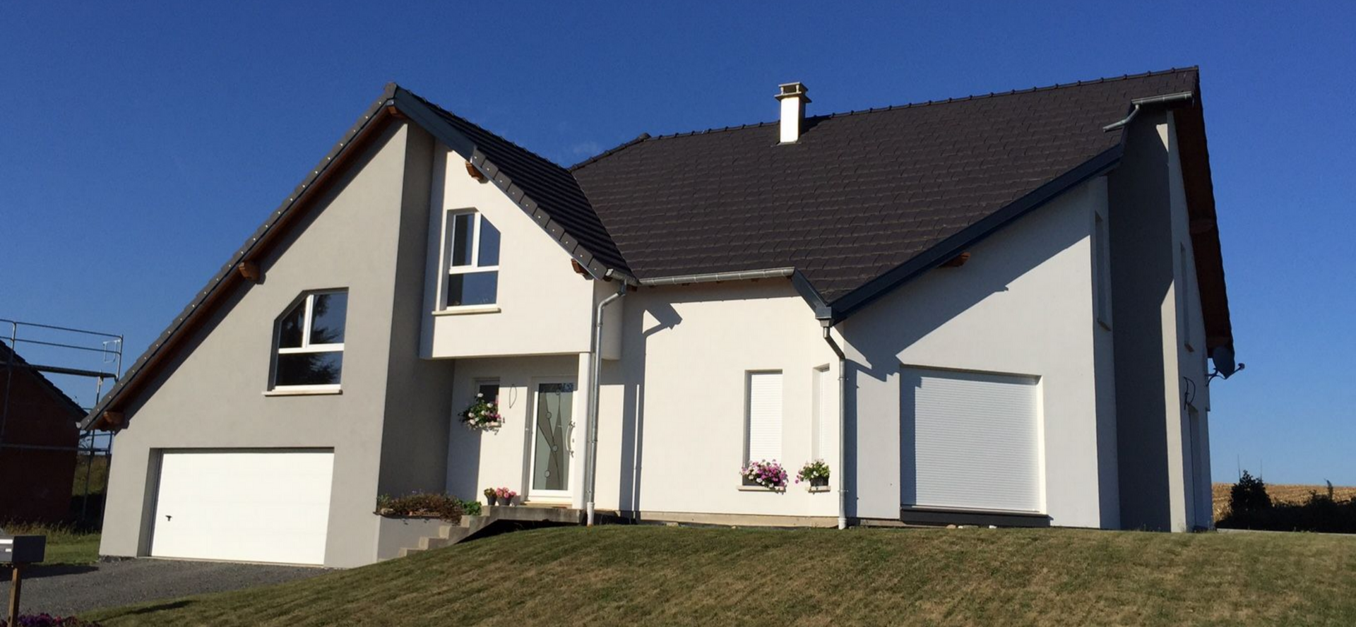 Une maison à deux étages avec un toit sombre et une porte de garage, se détachant sur un ciel bleu clair.