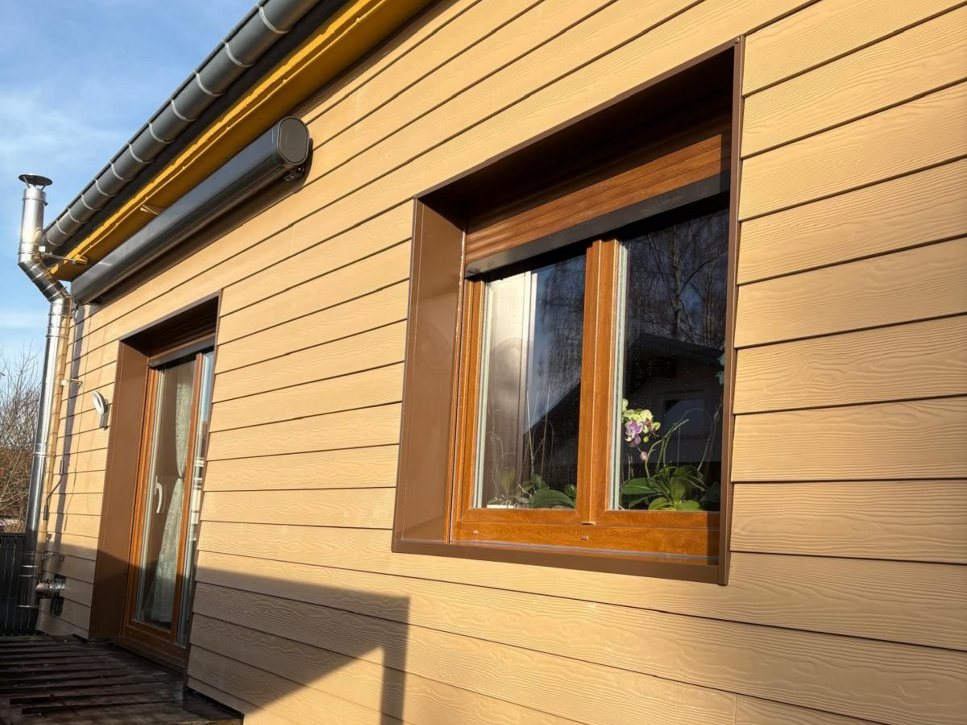 Bâtiment commercial gris et noir avec fenêtres et entrée sur une zone pavée, sous un ciel bleu.