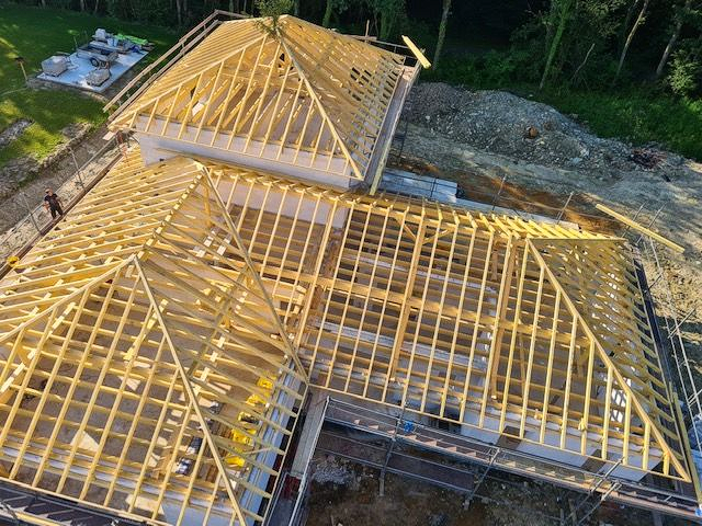 Charpente en bois du toit d'une maison en construction ; lumière naturelle et matériaux de construction visibles.