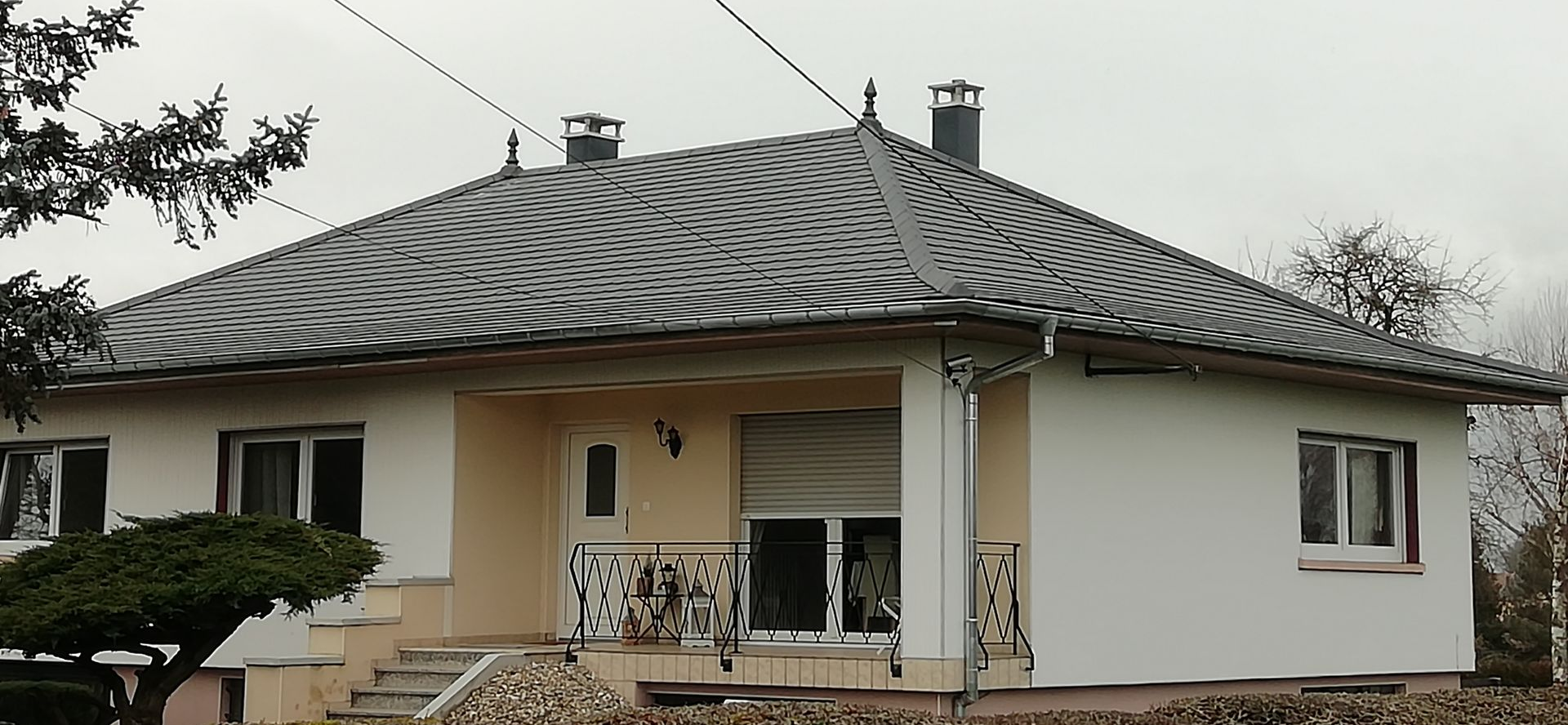 Une maison au toit à motifs et aux murs beiges se dresse sous un ciel nuageux.