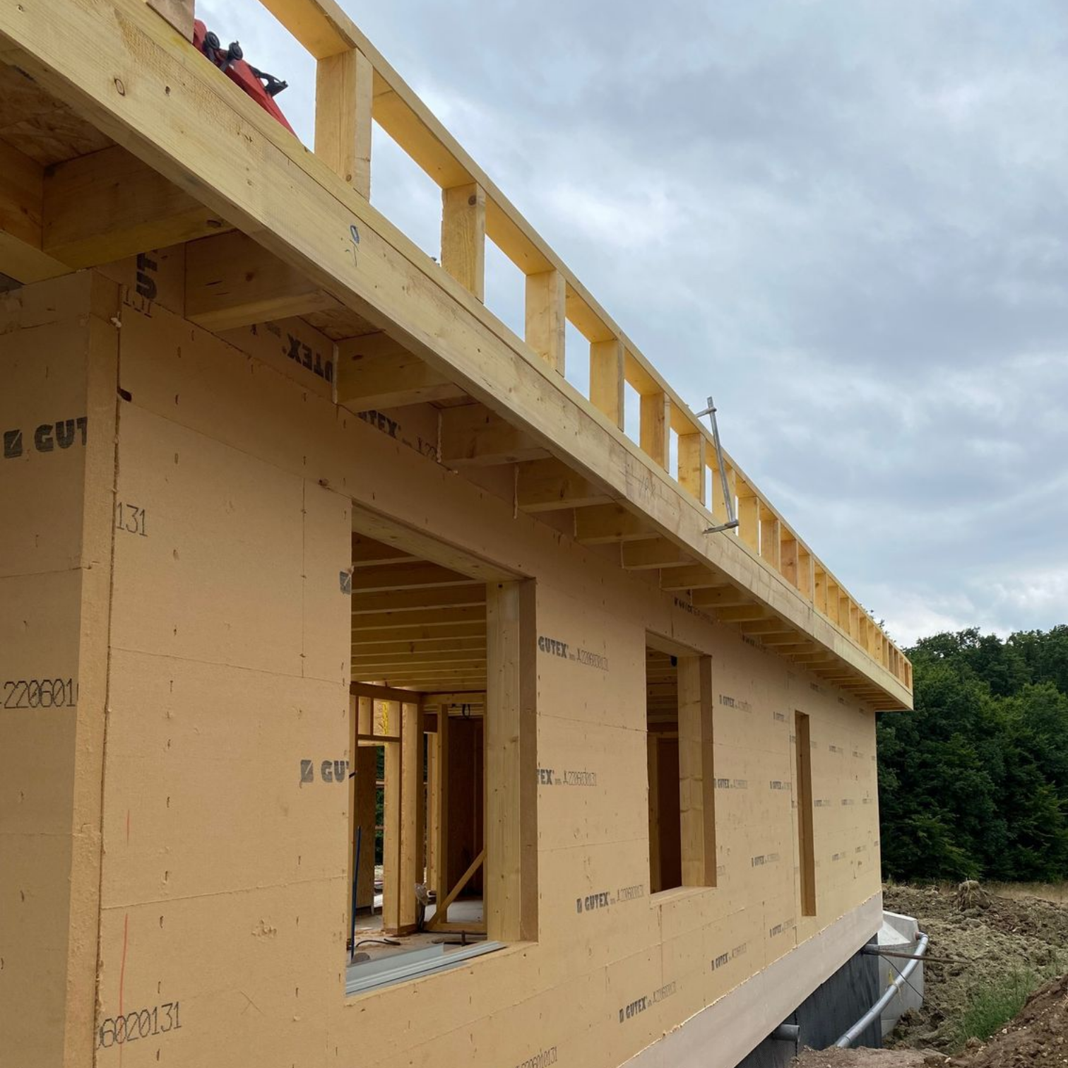 Intérieur d'une maison en construction avec une charpente en bois apparente et une fenêtre centrale.