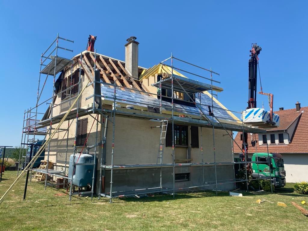 Maison en construction, échafaudages, grue, toiture partiellement remplacée.