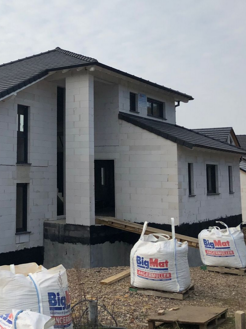 Maison en construction, vue extérieure, avec de grands sacs de matériaux de construction.