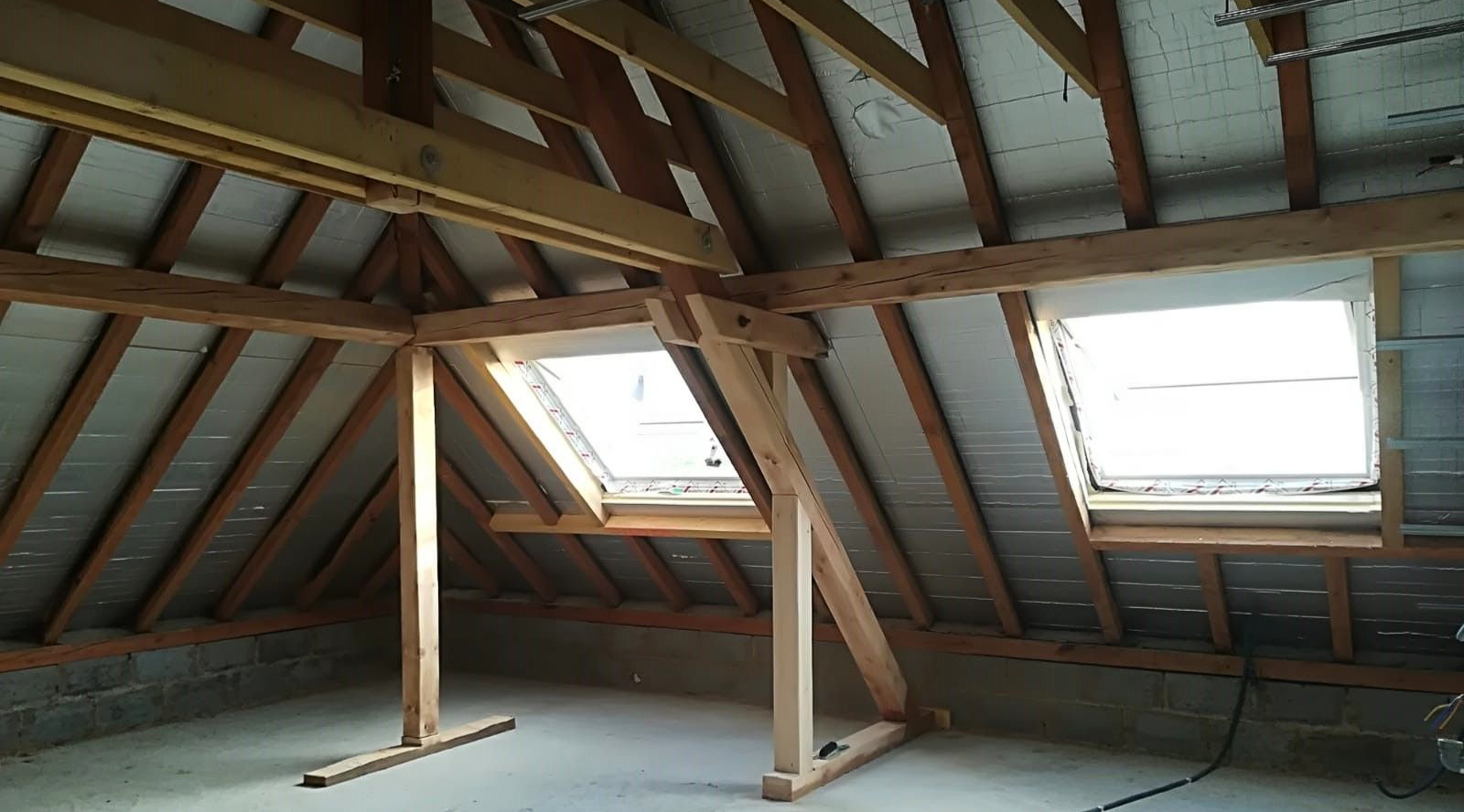 Vue intérieure d'un grenier avec puits de lumière, recouvert d'isolant et de matériaux de construction.