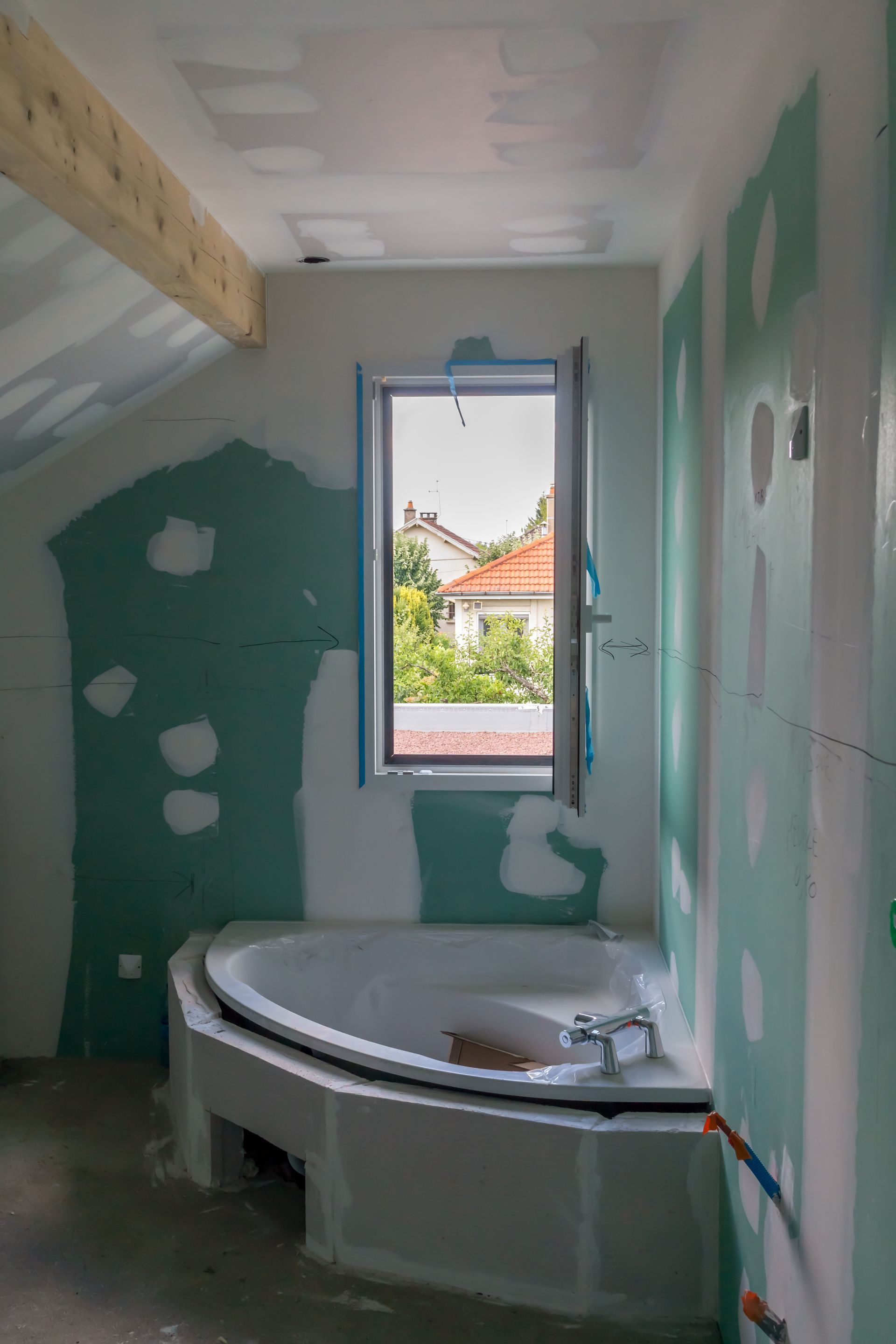 Salle de bain en construction, avec baignoire, fenêtre et cloisons sèches apparentes.