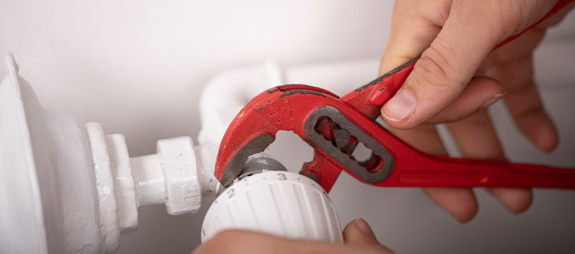 Une personne utilise une clé rouge pour tourner une vanne thermostatique blanche sur un radiateur.