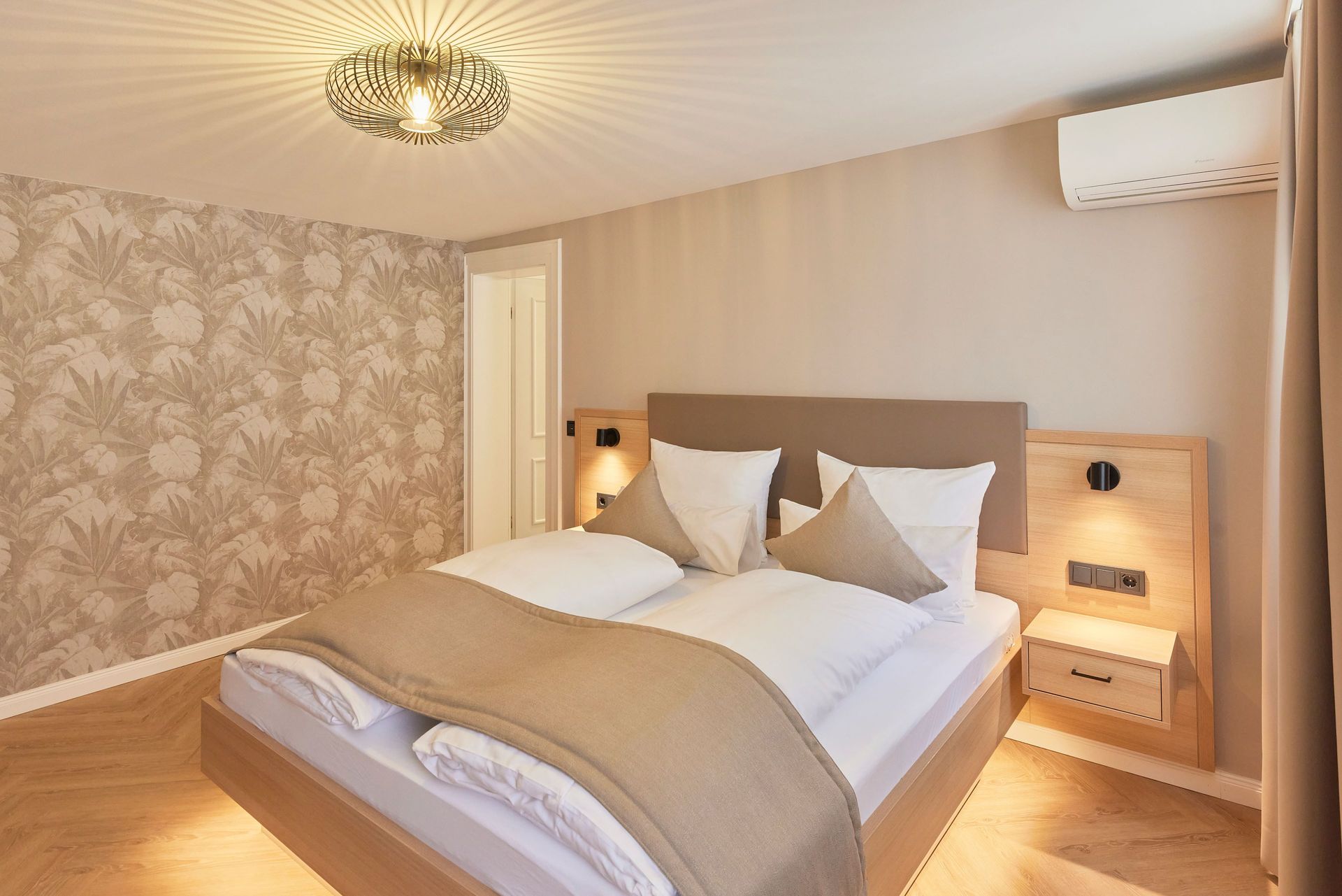 Schlafzimmer mit Doppelbett, beigen Wänden, gemusterter Tapete und moderner Beleuchtung.