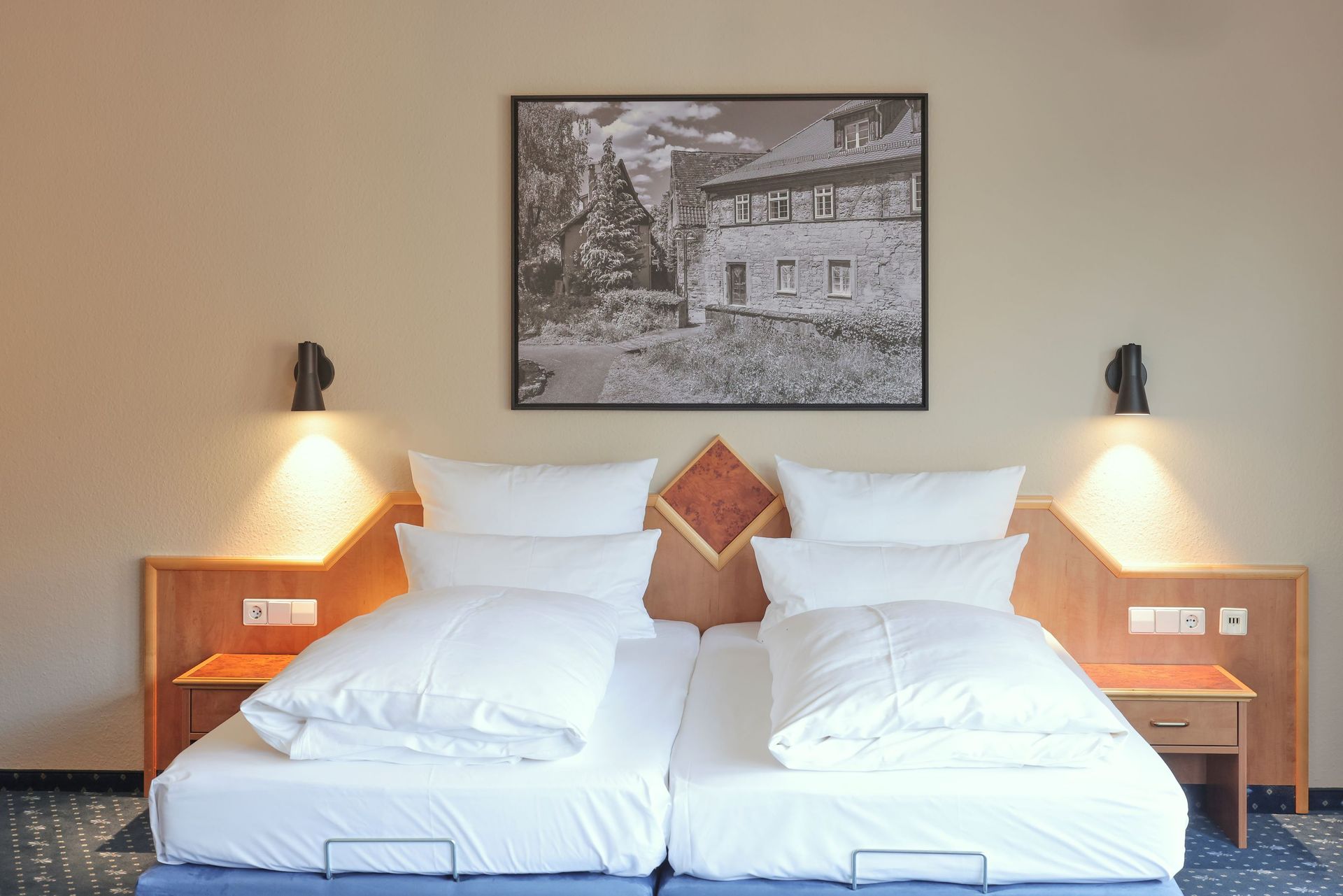 Zwei Einzelbetten mit weißer Bettwäsche, Nachttische, Lampen und ein gerahmtes Foto an der Wand.
