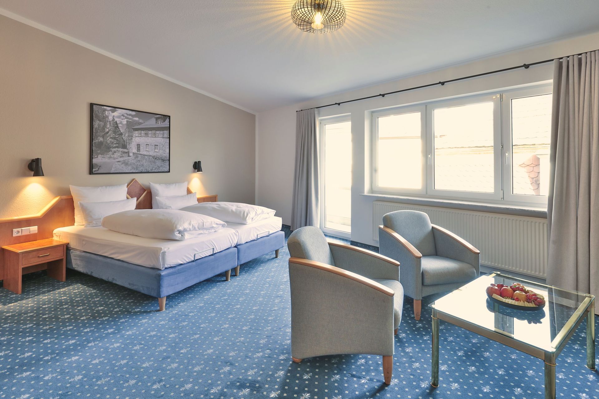 Hotelzimmer mit zwei Betten, zwei Sesseln, einem Tisch mit Obst und einem Fenster.