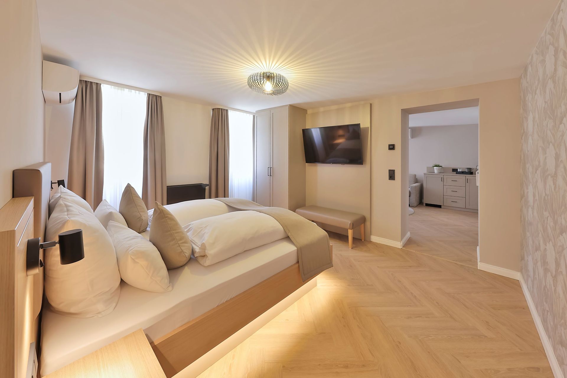 Modernes Hotelzimmer mit Bett, Fernseher und hellem Holzboden.