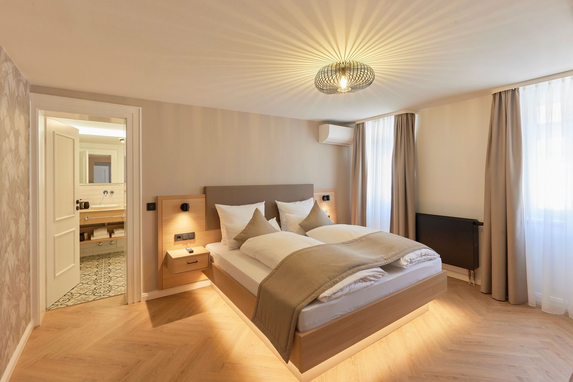 Schlafzimmer mit einem Bett, Nachttischen, einem Fenster und einer offenen Tür zu einem Badezimmer.