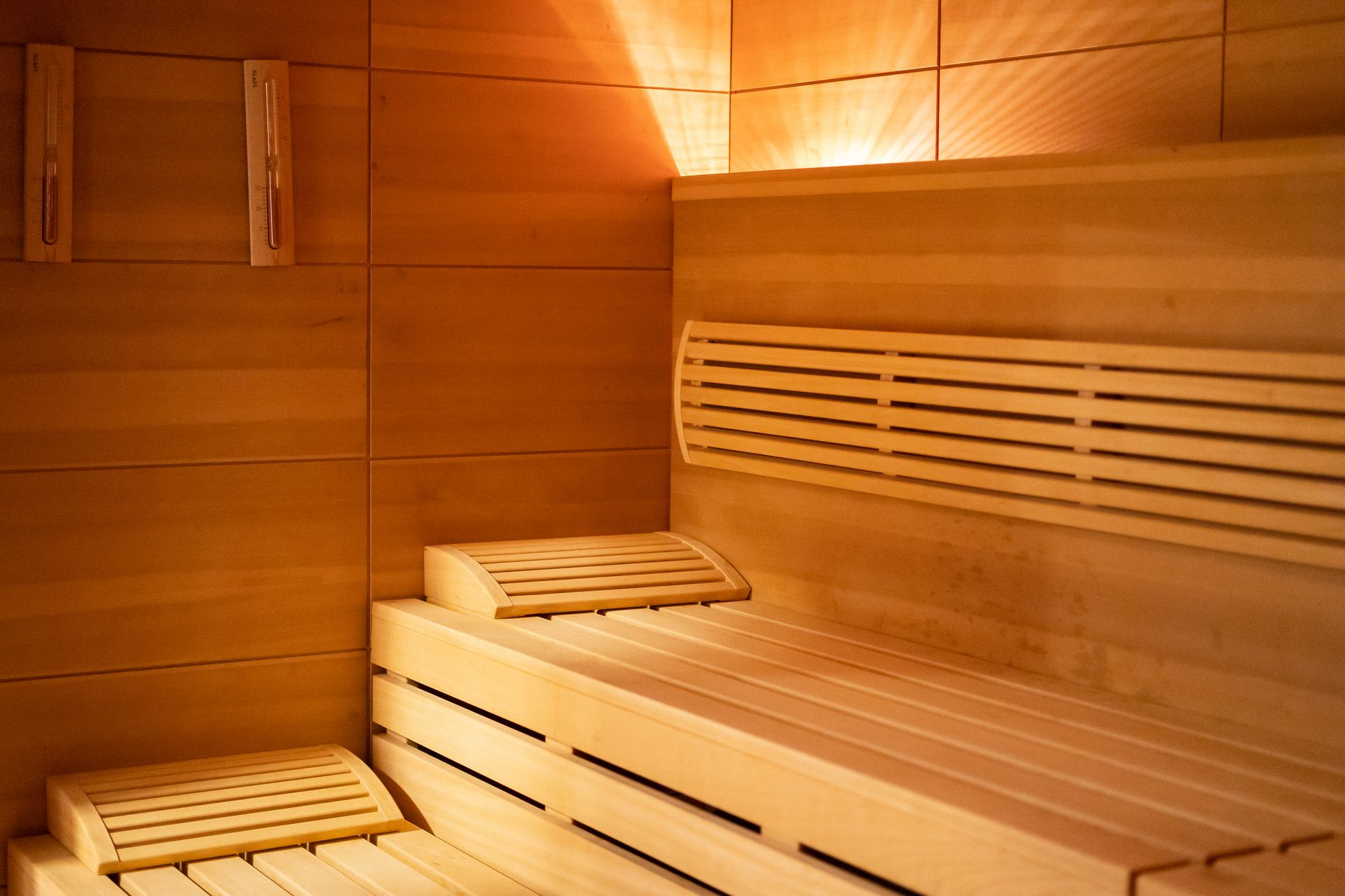 Saunainnenraum aus Holz mit Bänken und Wandverkleidung, beleuchtet von warmem Licht.
