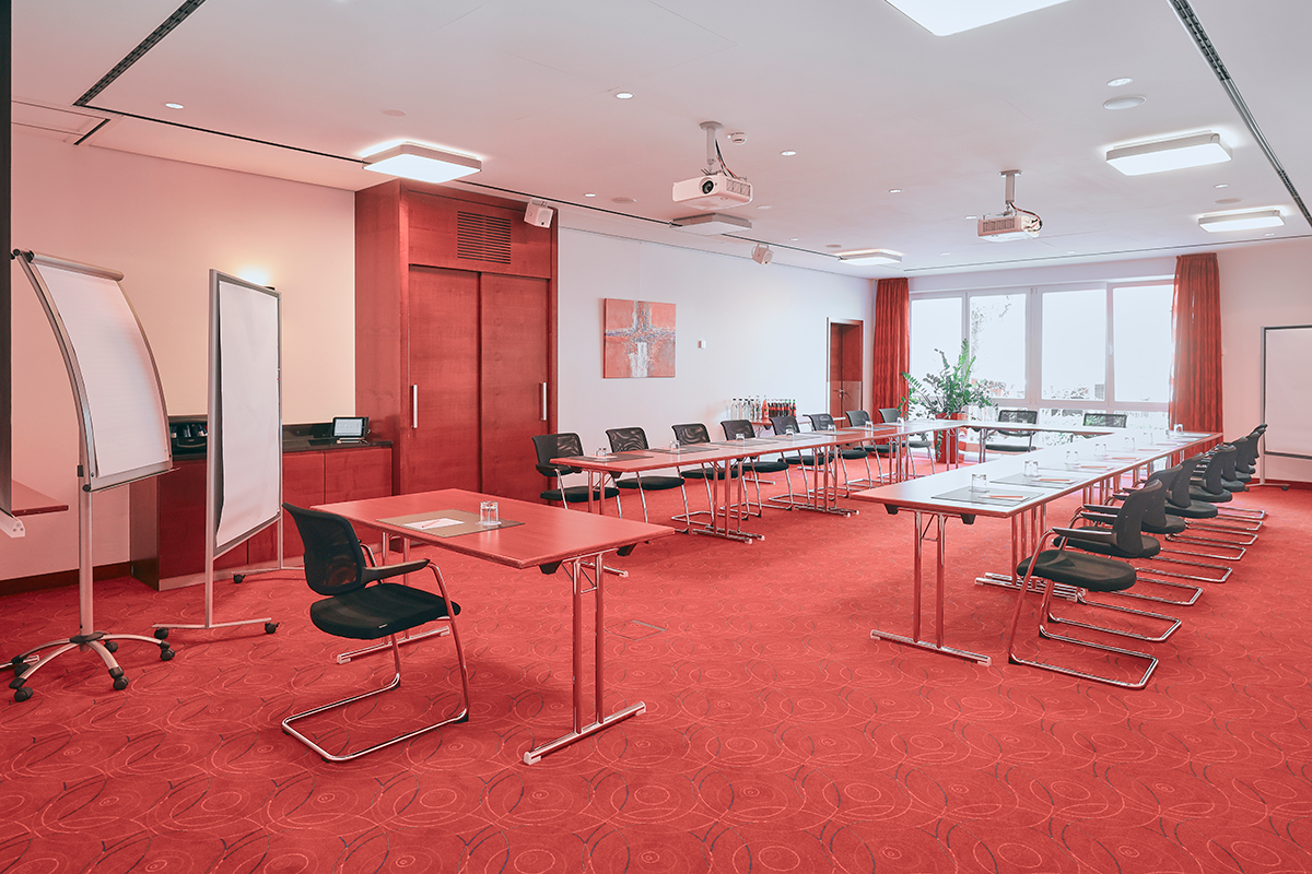 Konferenzraum mit rotem Teppich, Tischen, Stühlen und Whiteboards.